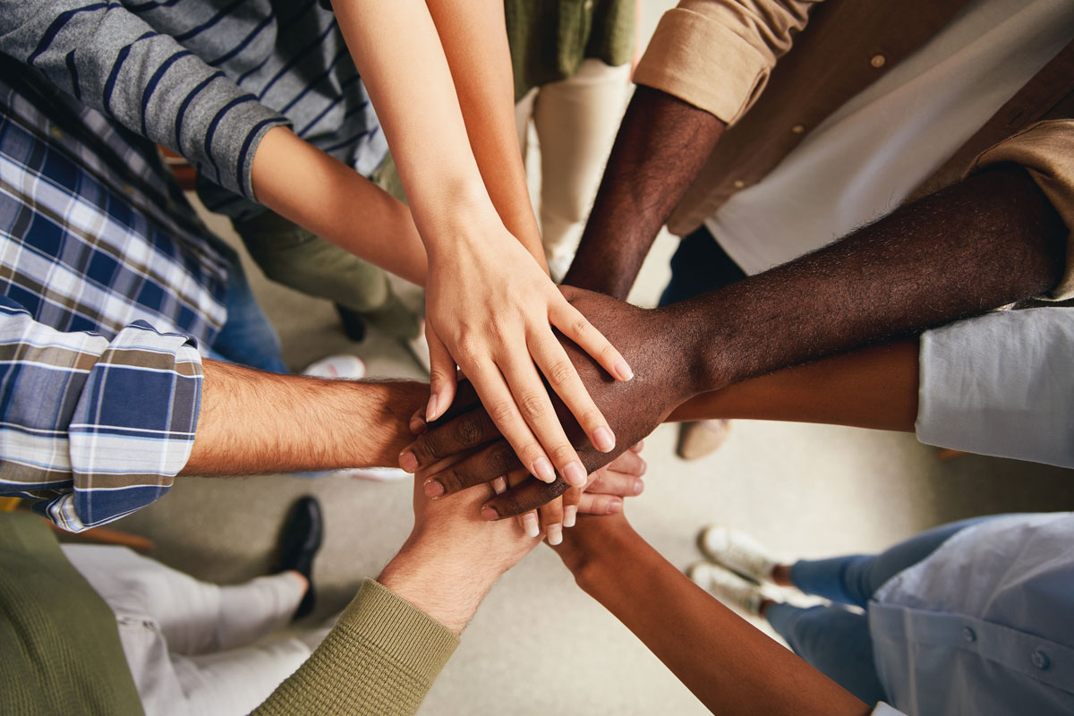 Stock photo of a group of people with varied skin tones putting their hands together.
